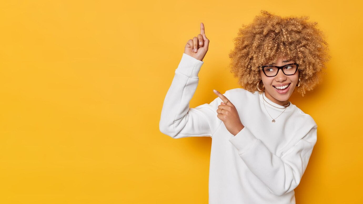 Yüz Hatlarının Gözlük Seçimindeki Önemi 1 Cheerful Curly Haired Adorable Woman Points Against Blank Space Shows Information Banner Demonstrates Advertisement Wears Spectacles White Casual Jumper Isolated Yellow Background 273609 60809